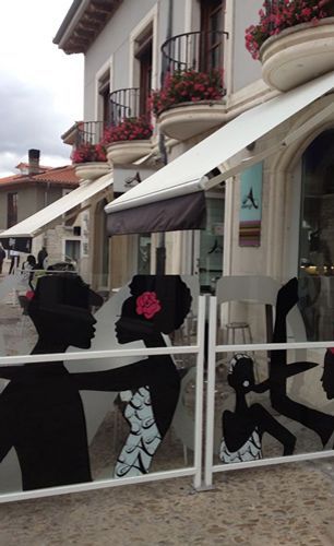 Una silueta de una mujer con una flor en el pelo está detrás de una valla frente a un edificio.