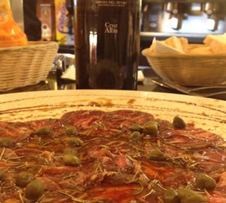 Un primer plano de una pizza con una botella de Casa Alta al fondo.