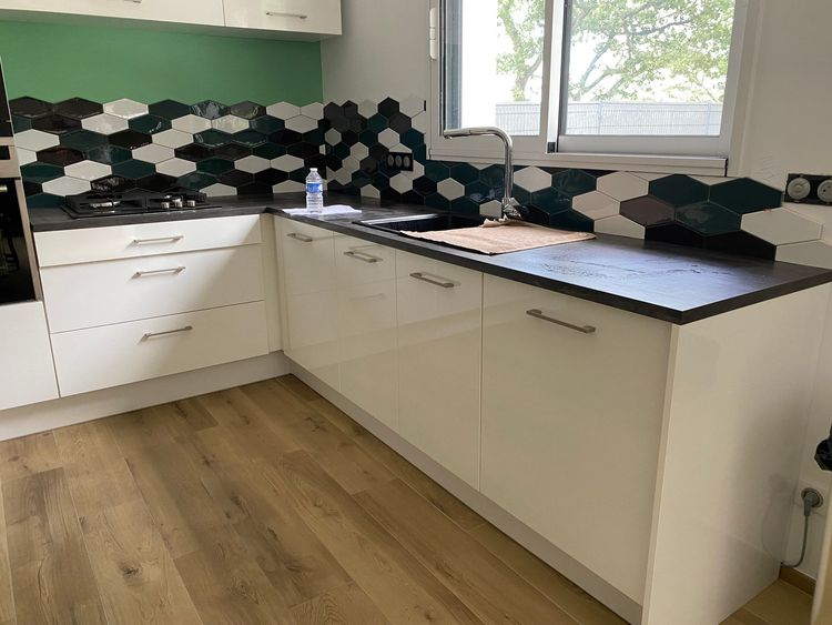 Cuisine moderne avec crédence carrelée, parquet et plans de travail.