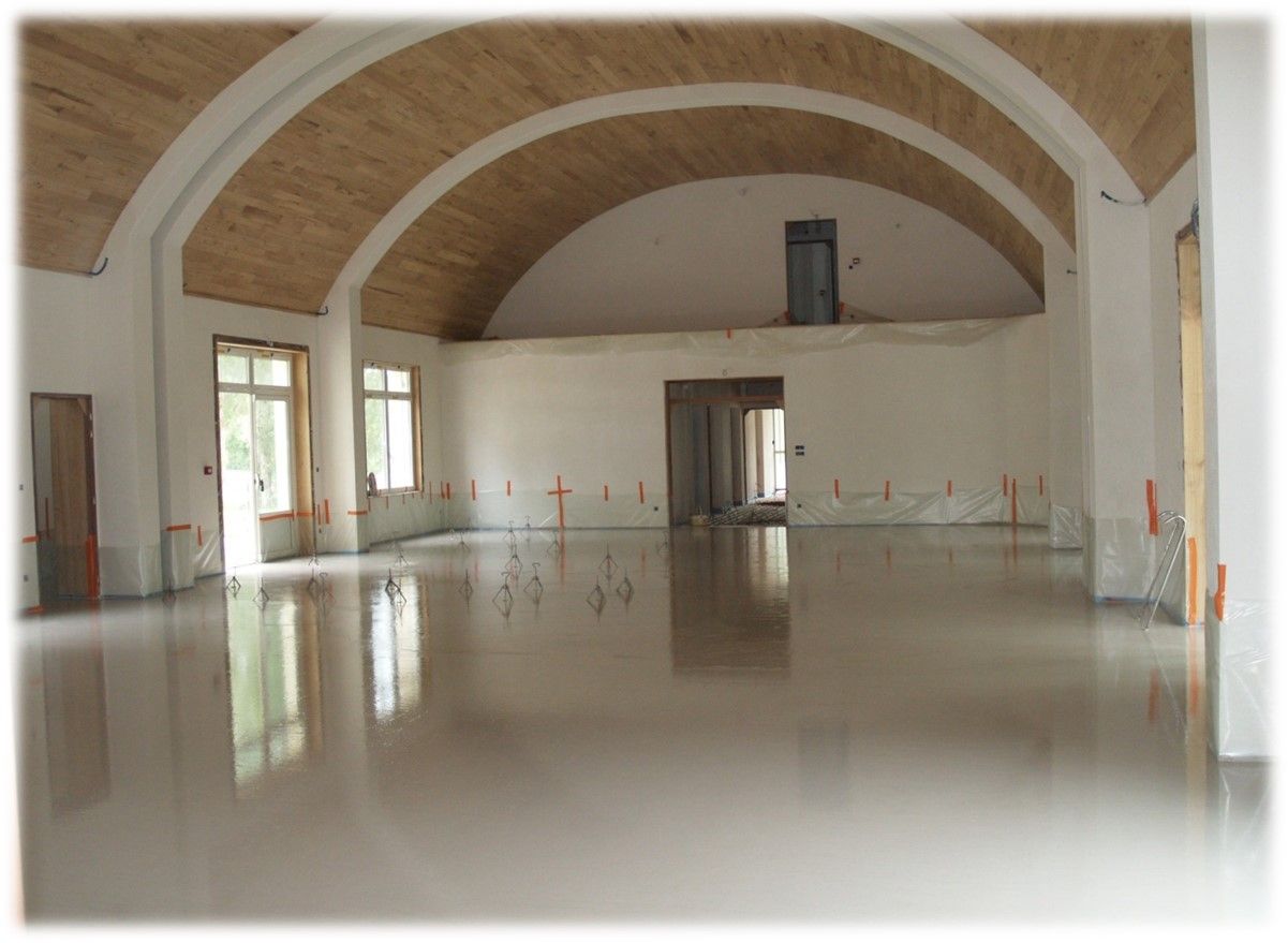 Hall vide avec plafond voûté, sol brillant et portes et fenêtres en bois au fond.