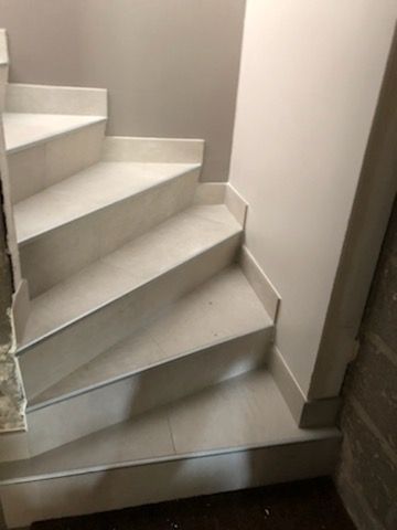 Escalier en colimaçon carrelé dans un coin intérieur étroit, murs et moulures.