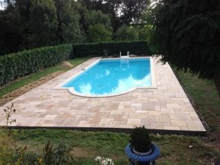 Piscine dans le jardin avec une terrasse en pierre et de hautes haies tout autour.