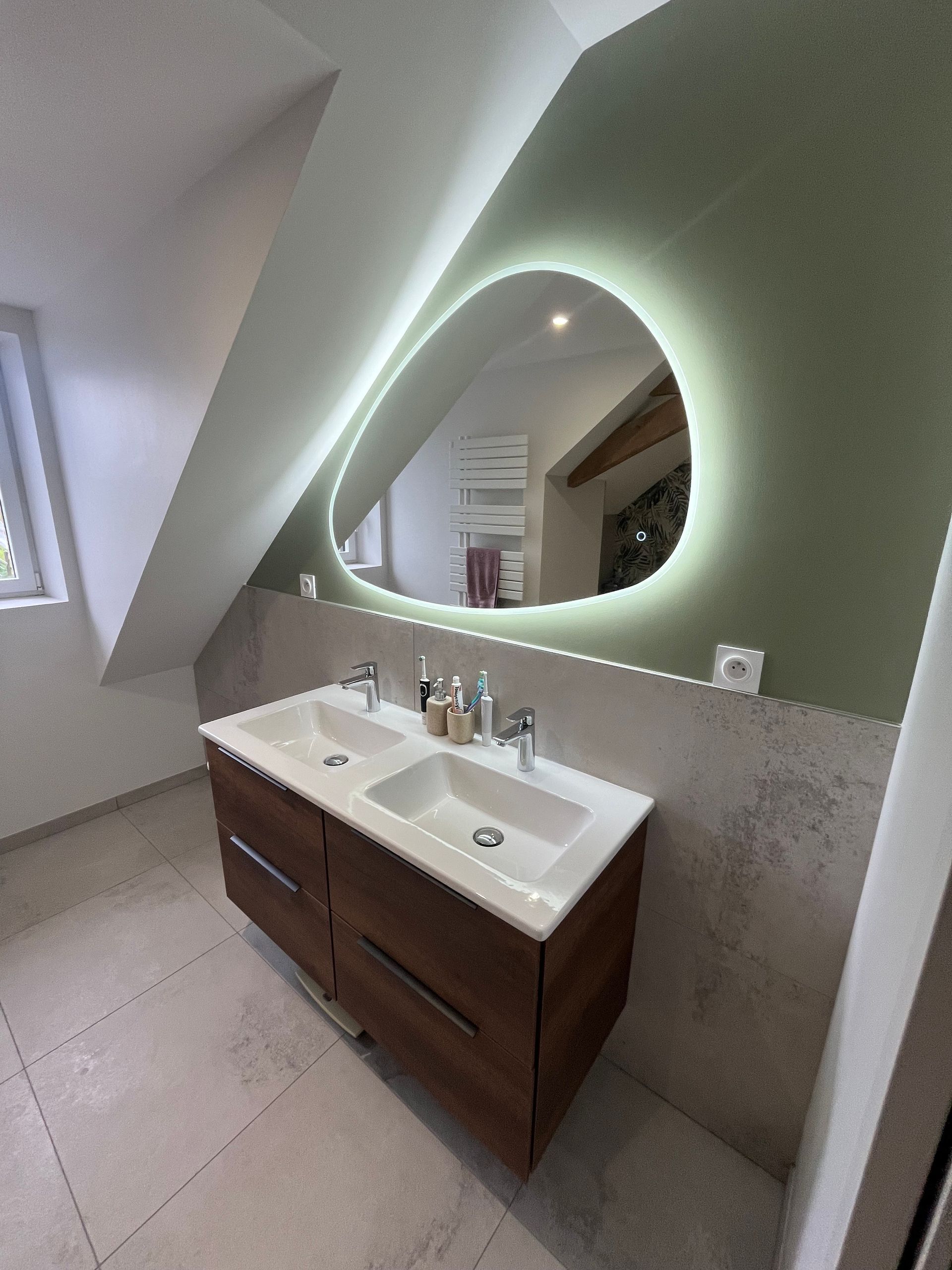 Salle de bains moderne avec miroir mural, lavabo et meuble lavabo sous un plafond mansardé.