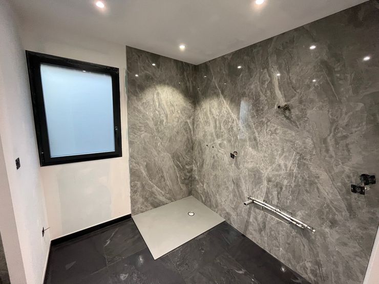 Salle de bains moderne avec carrelage en marbre, sol et petite fenêtre dépolie.