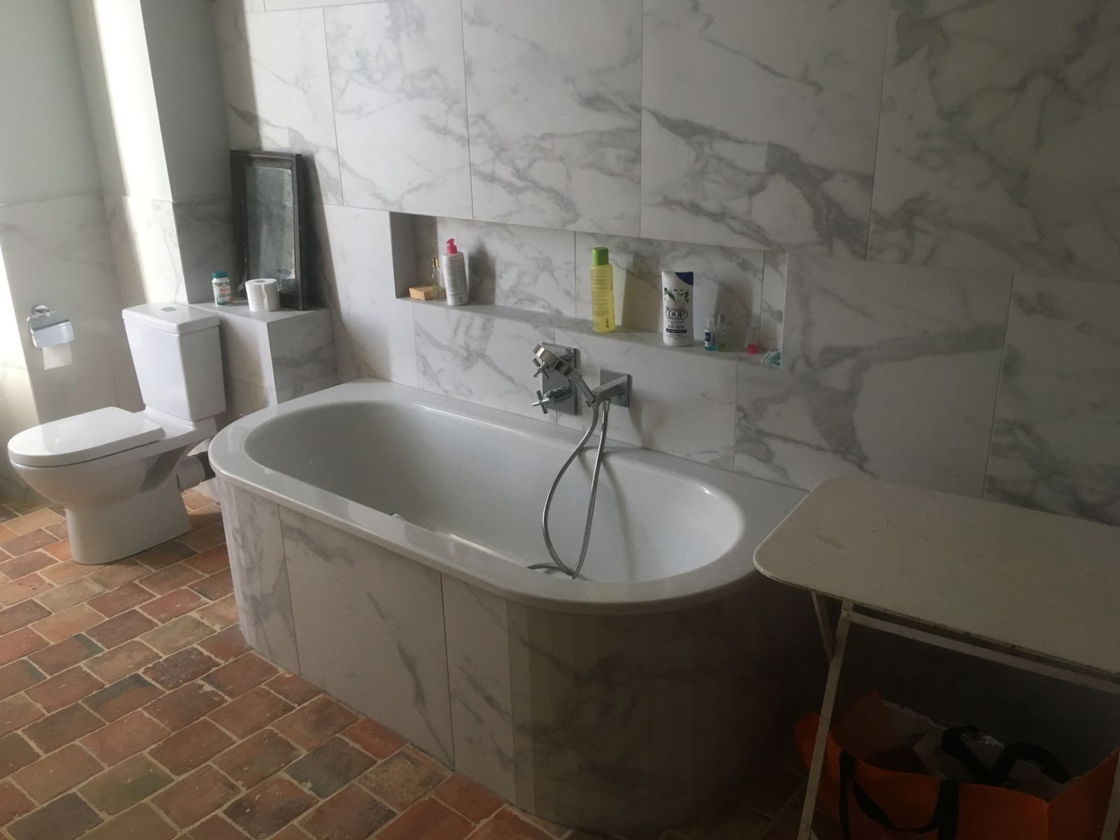 Salle de bains avec baignoire îlot, toilettes et sol carrelé près d'une fenêtre.