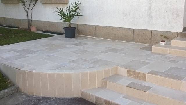 Terrasse avec dalles de pierre, marches et plante en pot contre un mur.