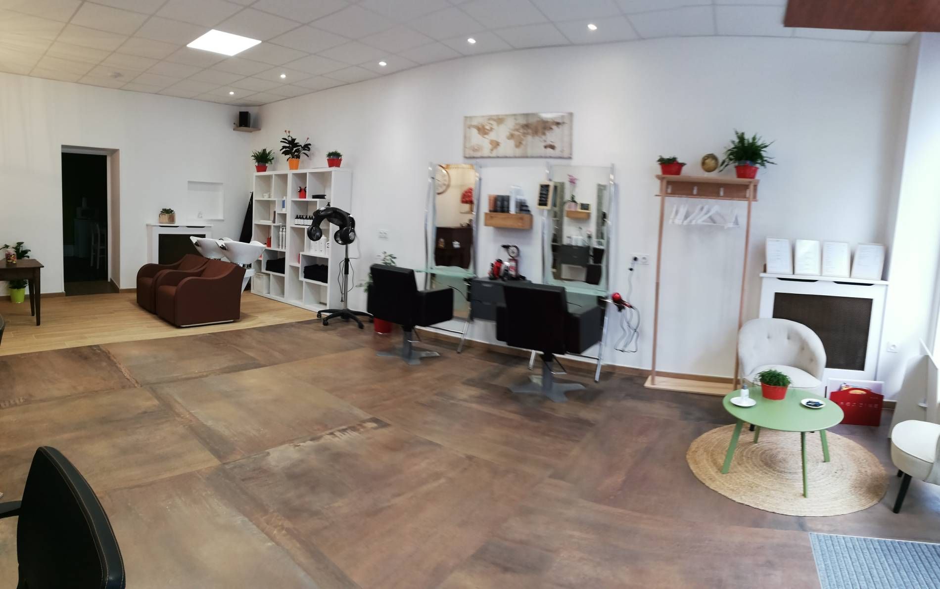 Salon spacieux et vide avec chaises, miroirs, étagères et petite table ronde sur un parquet.