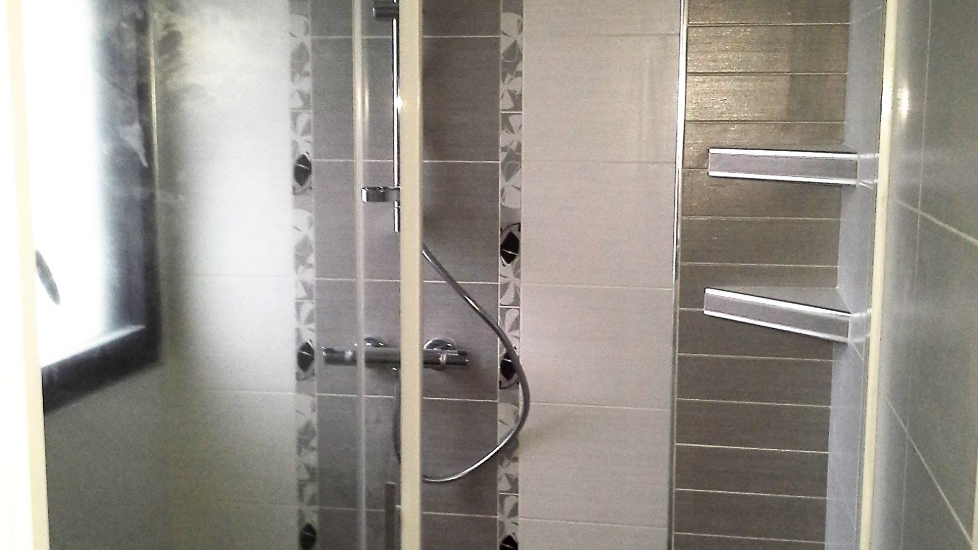 Douche moderne avec murs carrelés, portes en verre et étagères intégrées.