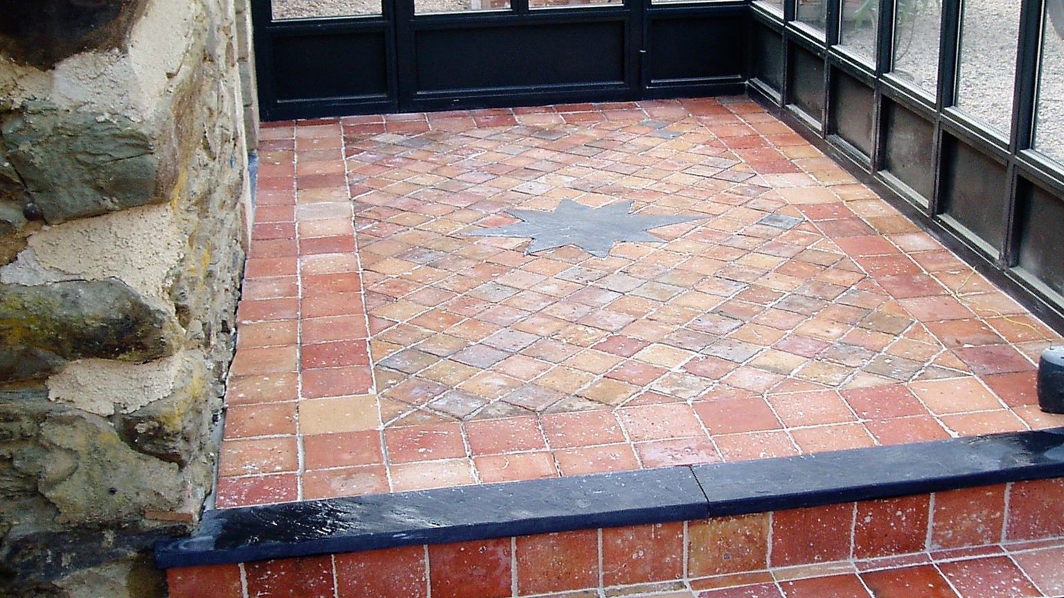 Petit patio carrelé avec un mur en pierre à gauche et des fenêtres.