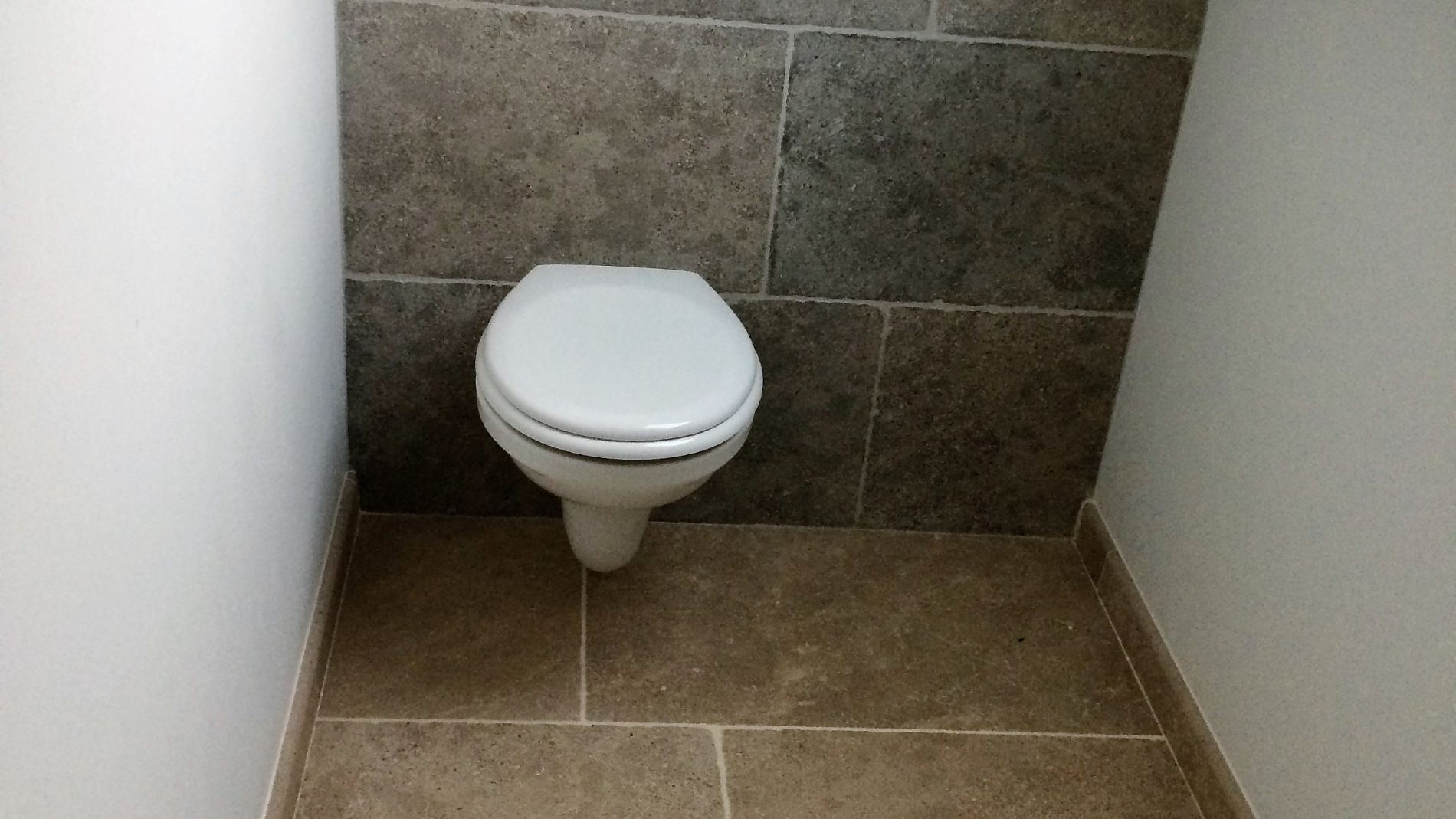 Petite toilette dans une cabine de toilettes d'angle carrelée.