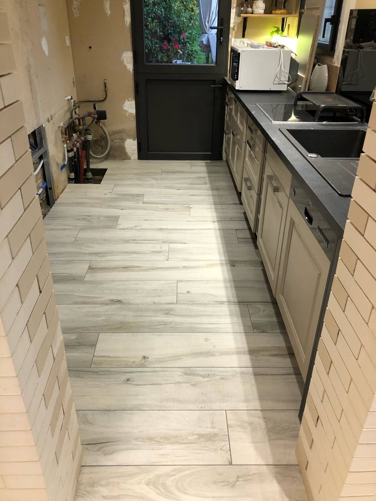 Cuisine étroite avec parquet, placards, plans de travail et murs en briques.