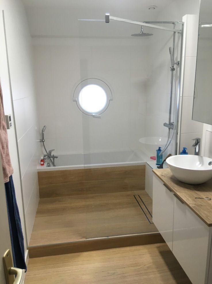 Salle de bains accessible avec baignoire à porte, fenêtre ronde et lavabo.