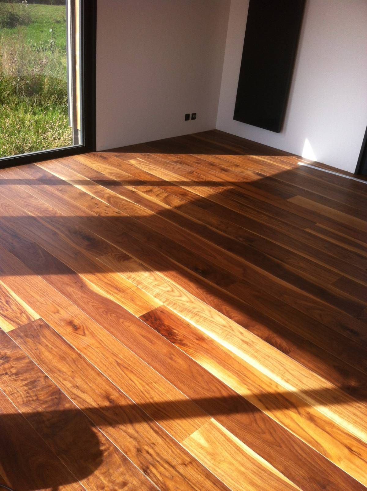 Pièce vide baignée de soleil, avec parquet ciré et grande fenêtre projetant des ombres.
