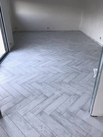 Pièce vide avec sol en carrelage à chevrons et murs, vue à travers une porte.