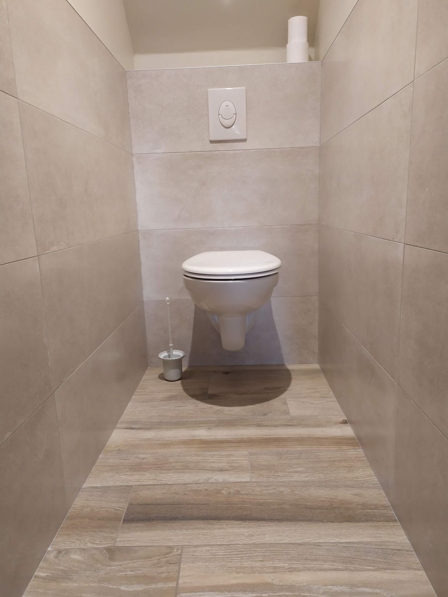 Petite salle de bains carrelée avec toilettes suspendues et mécanisme de chasse d'eau, vue depuis la porte.