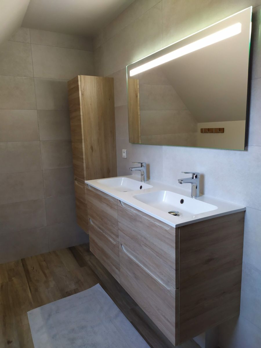 Salle de bains moderne avec meuble lavabo en bois, double vasque, grand miroir éclairé et murs carrelés.