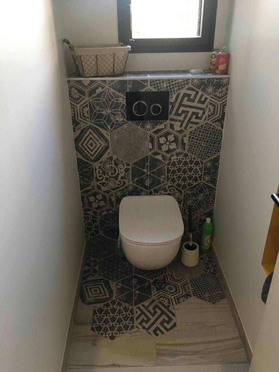 Petite salle de bains avec des toilettes, un mur carrelé à motifs et une fenêtre au-dessus.