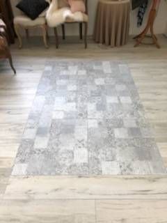 Tapis à carreaux sur un parquet dans une pièce avec des chaises et une table en arrière-plan.