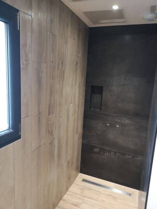 Cabine de douche moderne et étroite avec murs imitation bois, carrelage au fond et petite fenêtre sur la gauche.