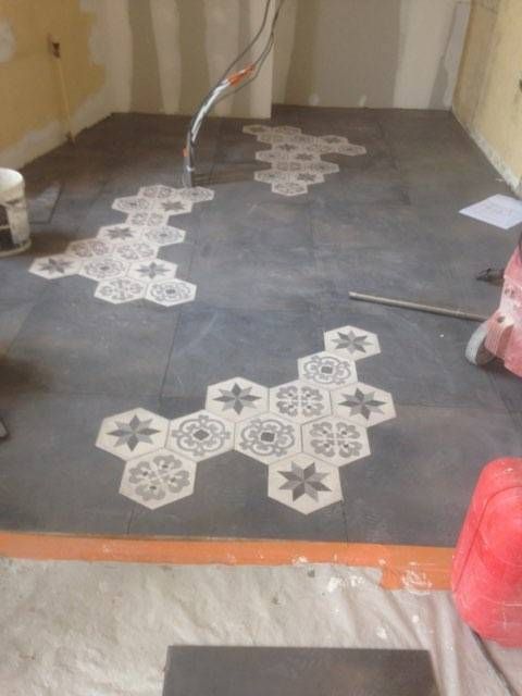 Sol intérieur d'une pièce avec des carreaux à motifs posés sur une surface, avec des outils et des fournitures à proximité.