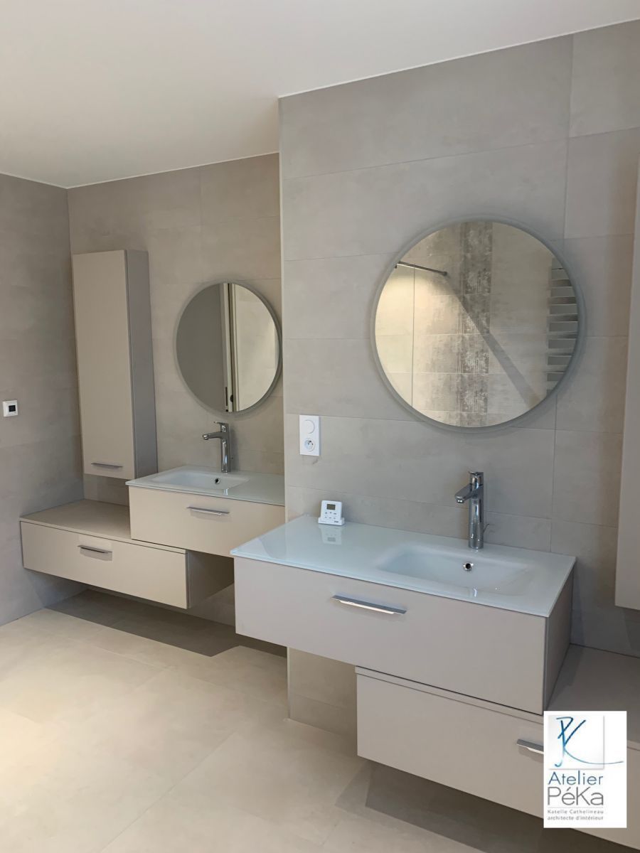 Salle de bains moderne avec deux lavabos suspendus, miroirs ronds, carrelage et une grande douche.