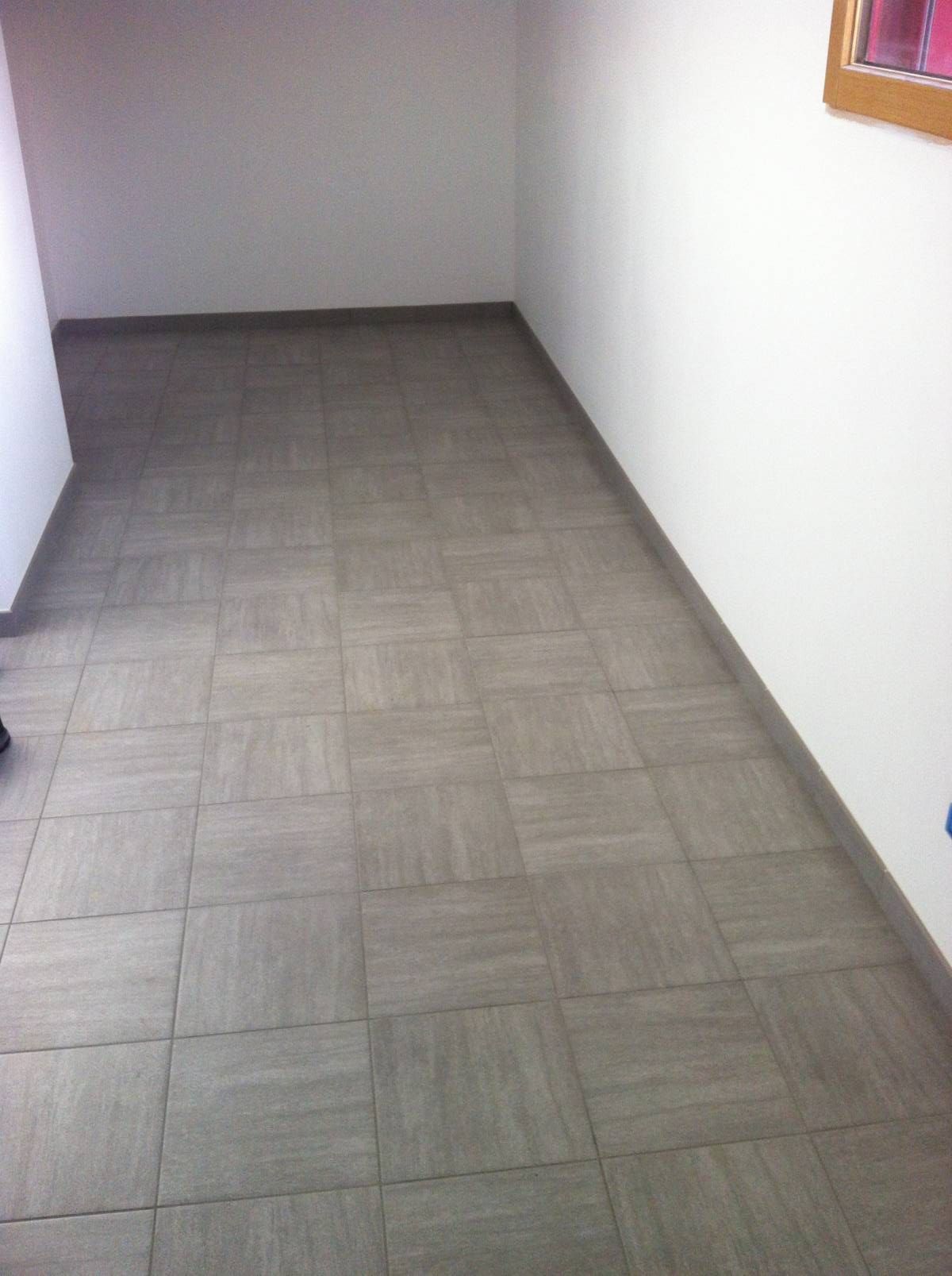 Couloir carrelé vide, aux murs et avec une fenêtre au fond.