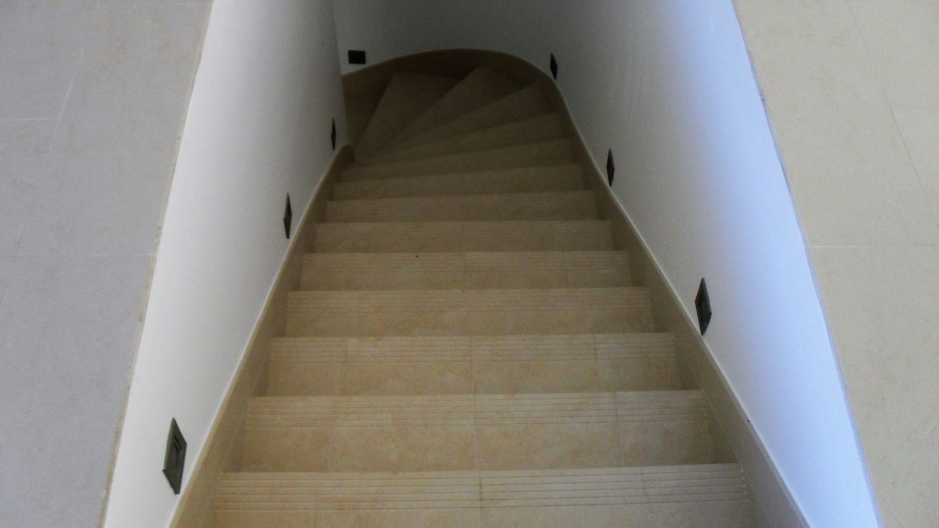 Escalier étroit recouvert de moquette, aux murs, menant à une ouverture.