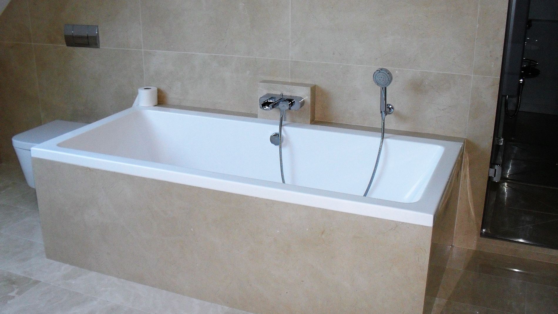 Baignoire encastrée avec entourage en carrelage et douchette à main dans une salle de bains.