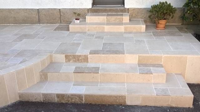 Terrasse en dalles de pierre avec des marches en bloc menant à un palier surélevé, à côté d'une plante en pot.