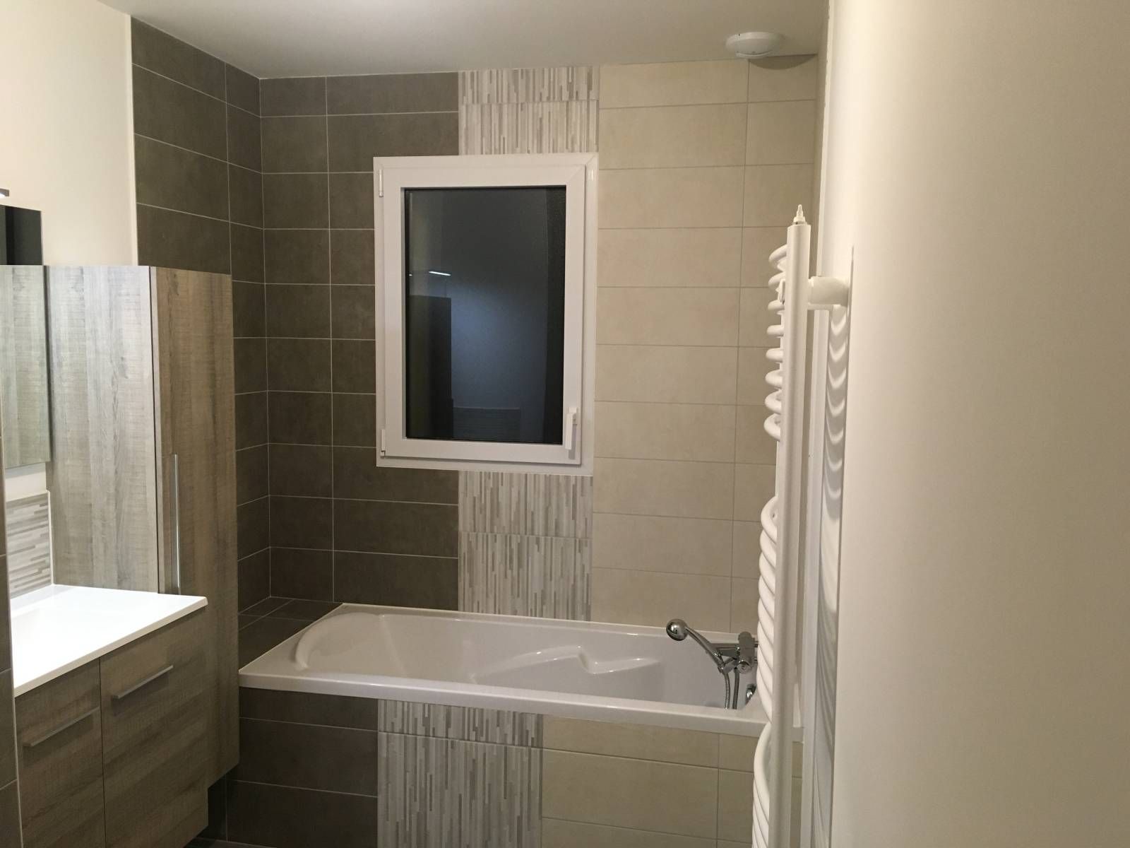 Salle de bains avec baignoire, murs carrelés, lavabo et petite fenêtre au-dessus de la baignoire.
