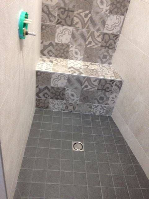 Petite cabine de douche carrelée avec sol, mur du fond à motifs et un seul robinet de douche.