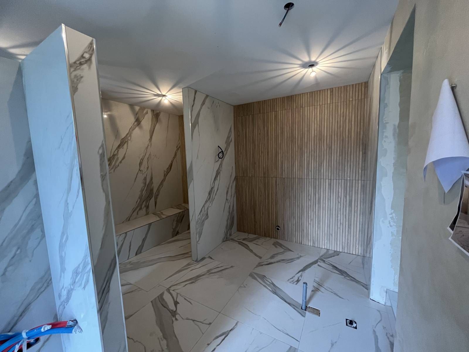 Salle de douche moderne avec murs et sol carrelés imitation marbre, spots au plafond et une serviette accrochée à droite.