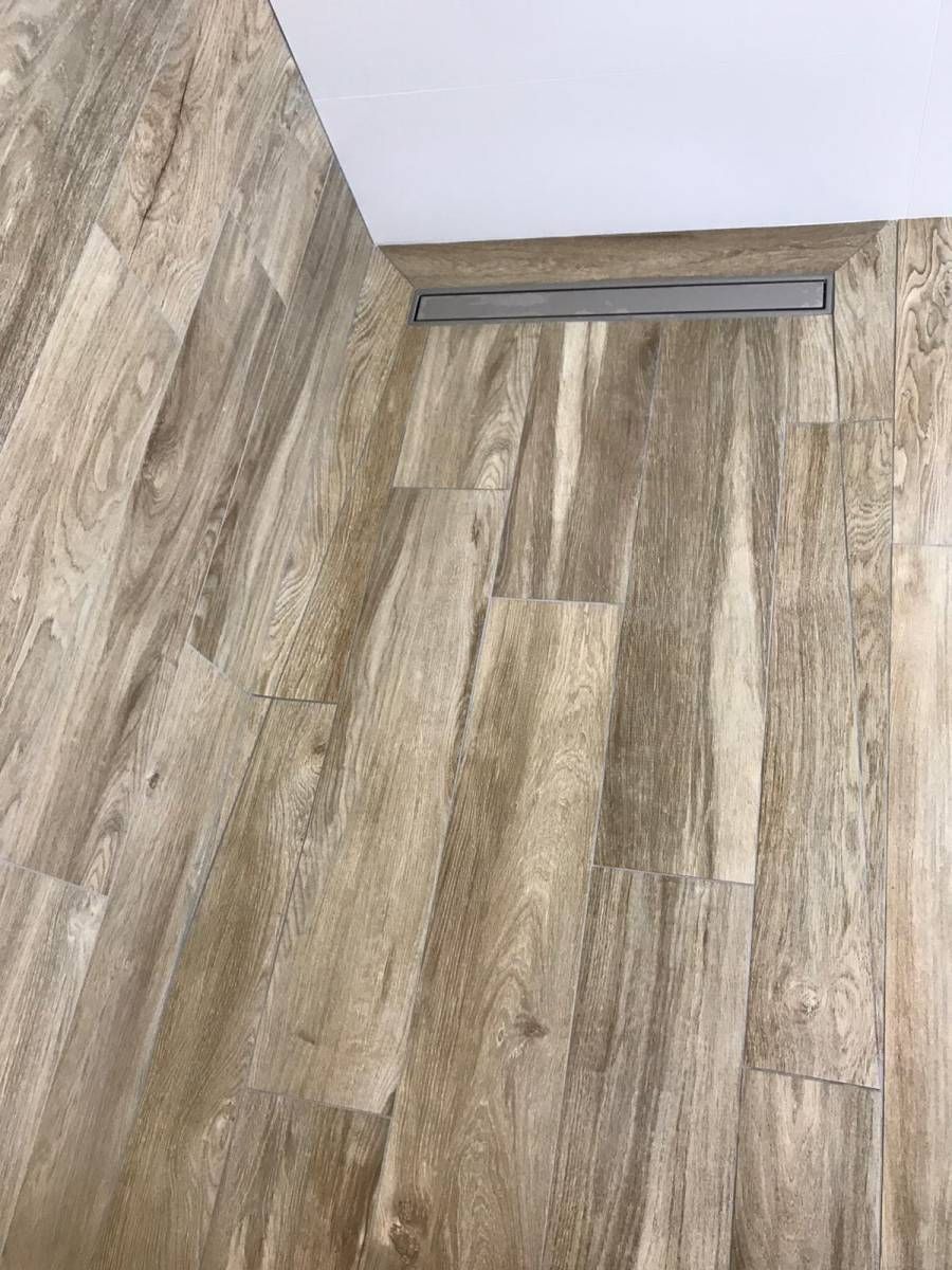 Carrelage imitation bois au sol, rejoignant un mur et un seuil de porte avec plinthes.