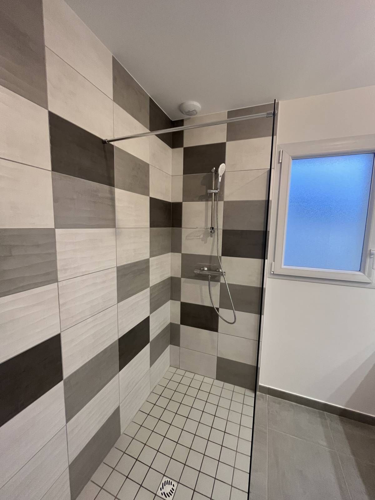 Douche à l'italienne carrelée avec murs, petit sol en mosaïque et fenêtre dépolie.