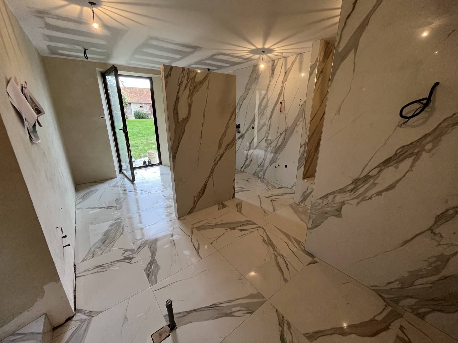 Pièce au sol en marbre, ornée de grands panneaux muraux en marbre et d'une porte ouverte donnant sur un espace extérieur gazonné.