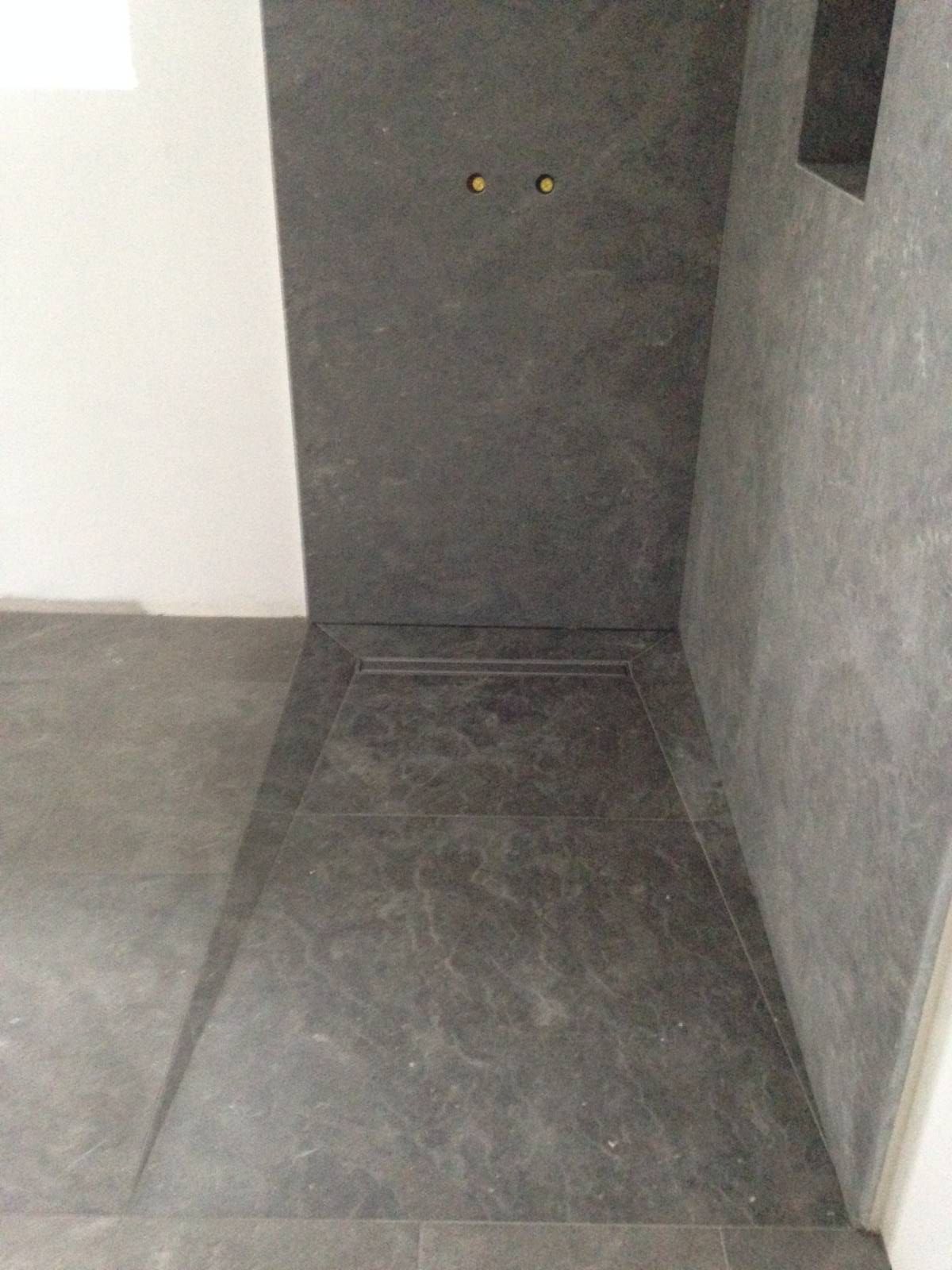 Pièce vide, aux murs et au sol en béton brut, avec une porte ou un panneau sombre au fond.