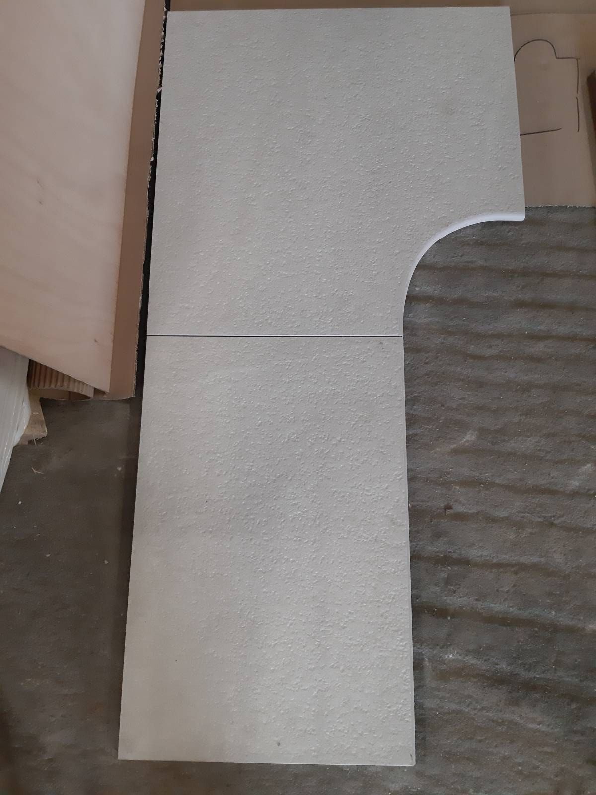 Des dalles de moquette posées en forme de L sur un sol, avec une découpe incurvée en haut à droite.