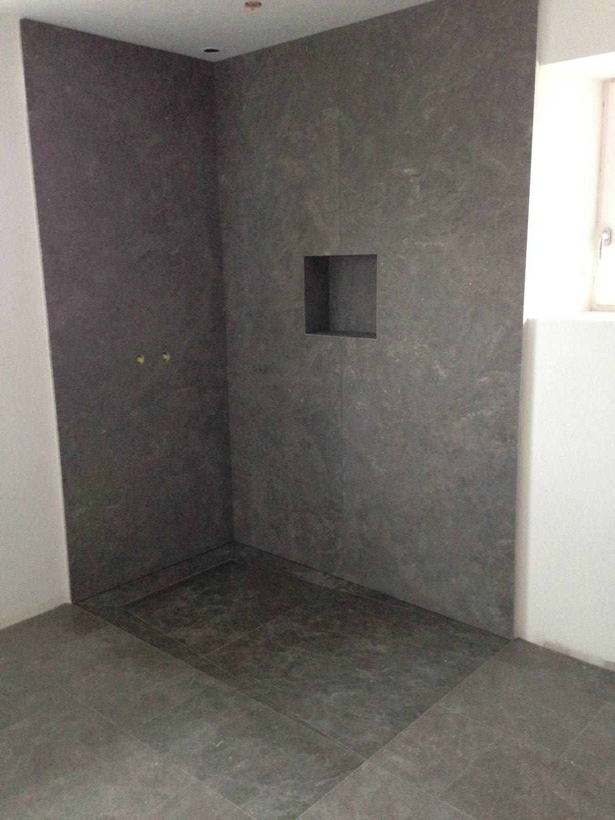 Cabine de douche vide, carrelée, avec une petite niche encastrée et des murs.