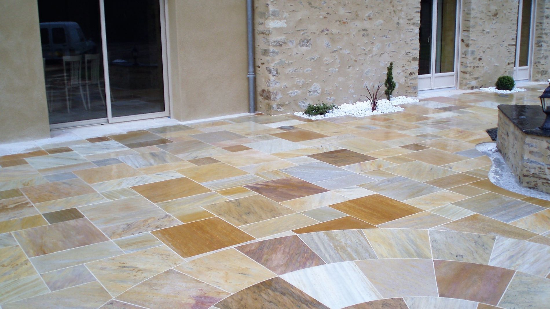 Terrasse en pierre avec carrelage à côté d'un bâtiment et de portes vitrées.