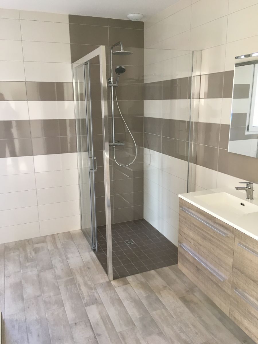 Salle de bains moderne avec douche à l'italienne, carrelage et meuble lavabo en bois.