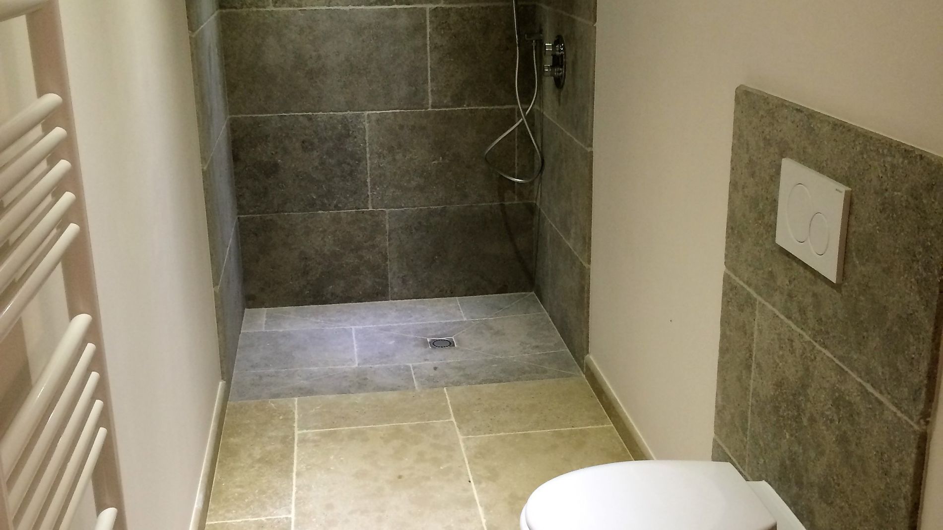 Cabine de salle de bains étroite carrelée avec toilettes et murs carrelés, vue depuis la porte.