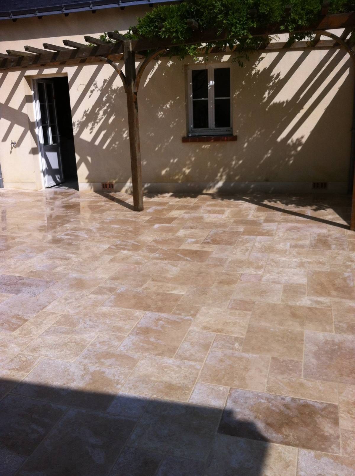 Cour ensoleillée avec terrasse carrelée, mur, fenêtre, porte ouverte et pergola projetant des ombres.