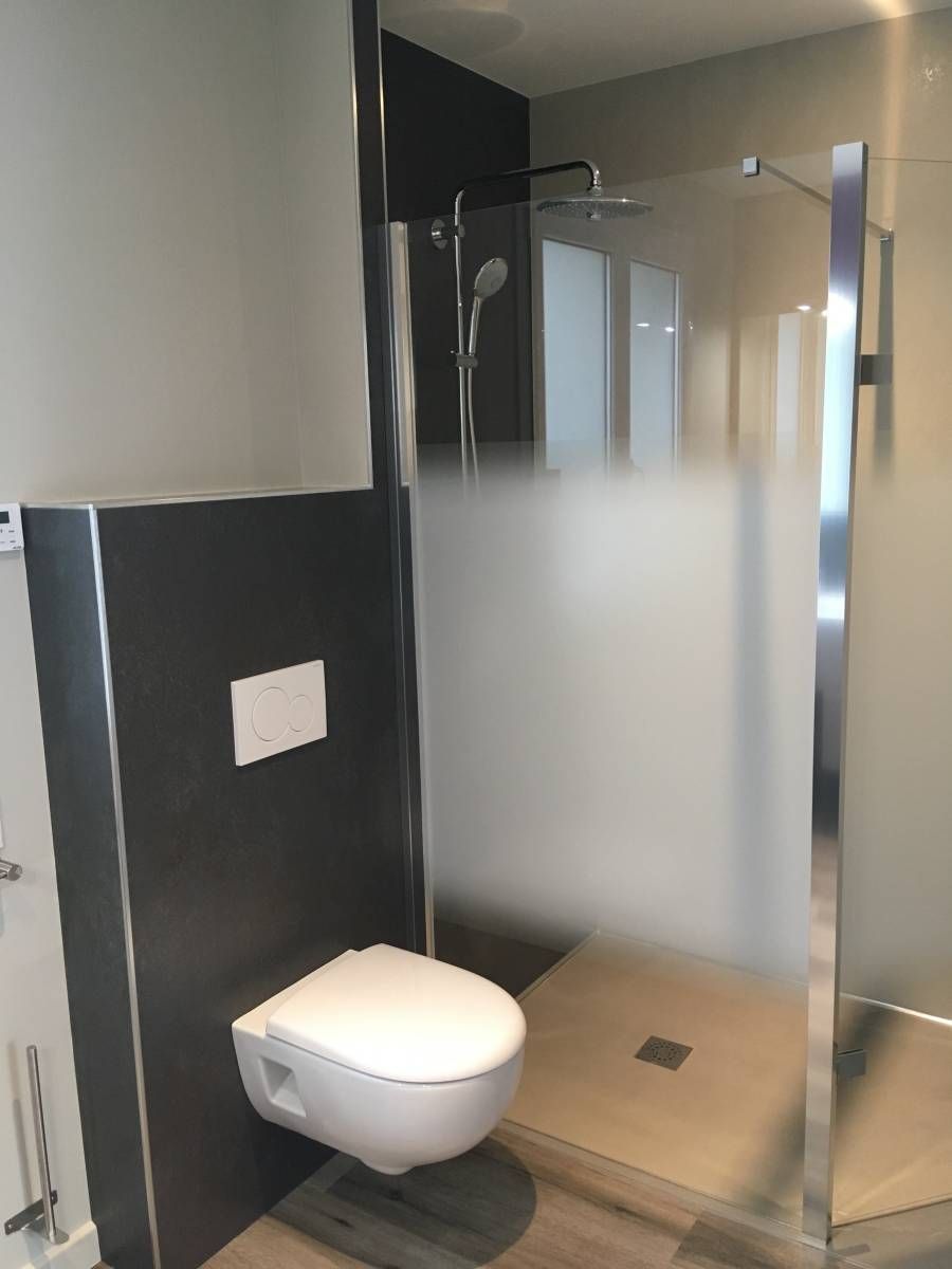 Salle de bains moderne avec toilettes suspendues et cabine de douche en verre, murs carrelés.