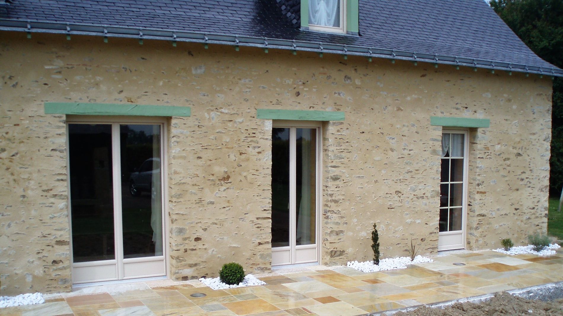 Maison en pierre avec murs, toit et nombreuses portes et fenêtres.