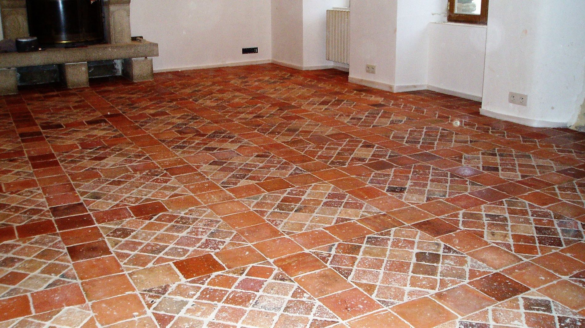 Pièce vide avec sol carrelé et murs, plus une cheminée sur la gauche.