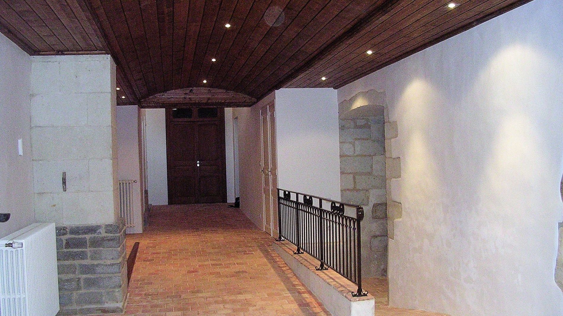 Couloir étroit aux murs, plafond en bois, sol carrelé et rambarde sur un côté.