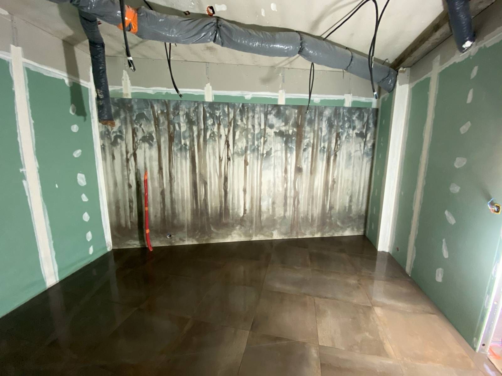 Pièce vide et inachevée avec des cloisons sèches, des bâches en plastique et un sol en béton humide.
