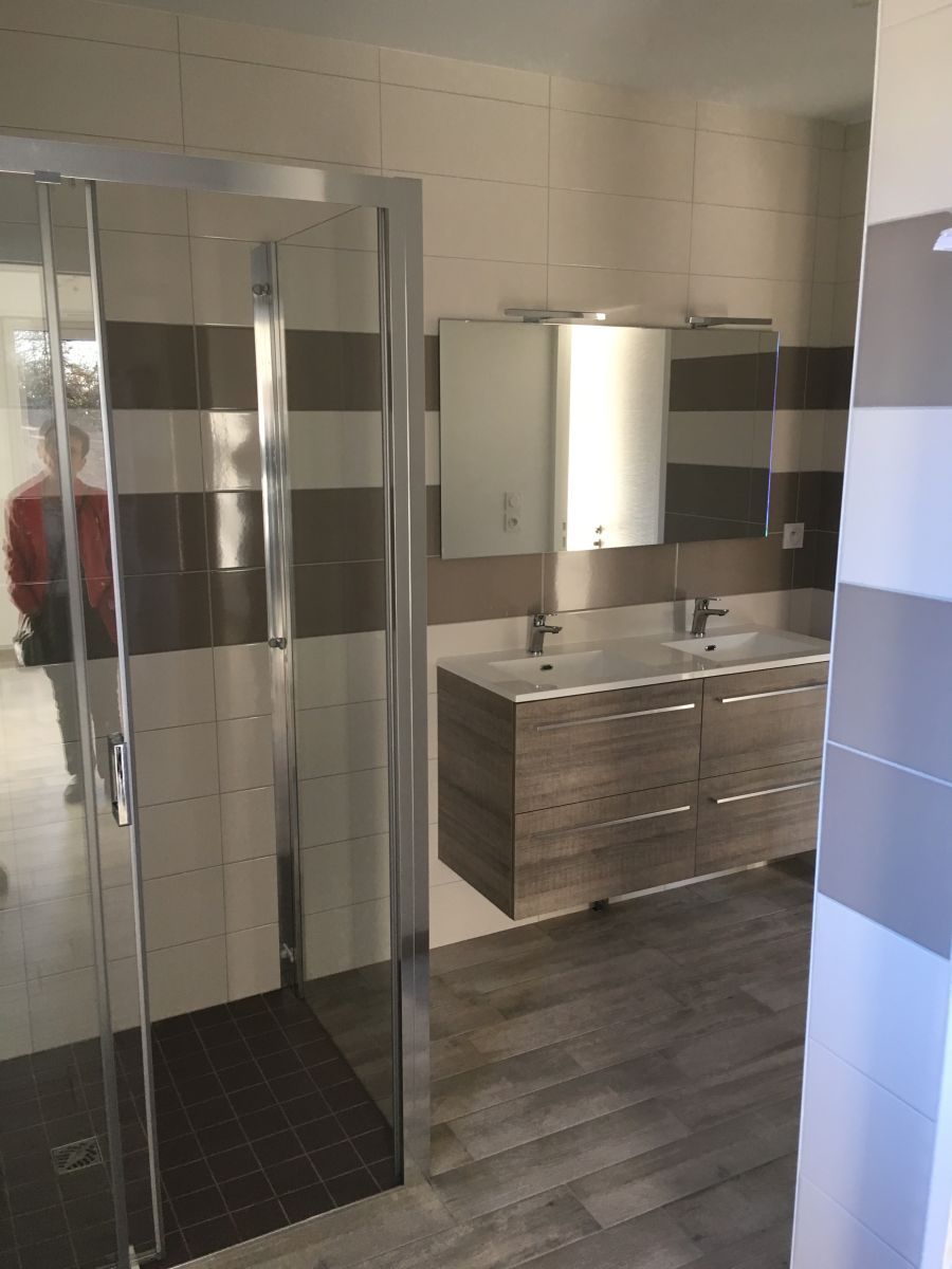 Salle de bains moderne avec douche en verre, meuble-lavabo, miroir et carrelage.