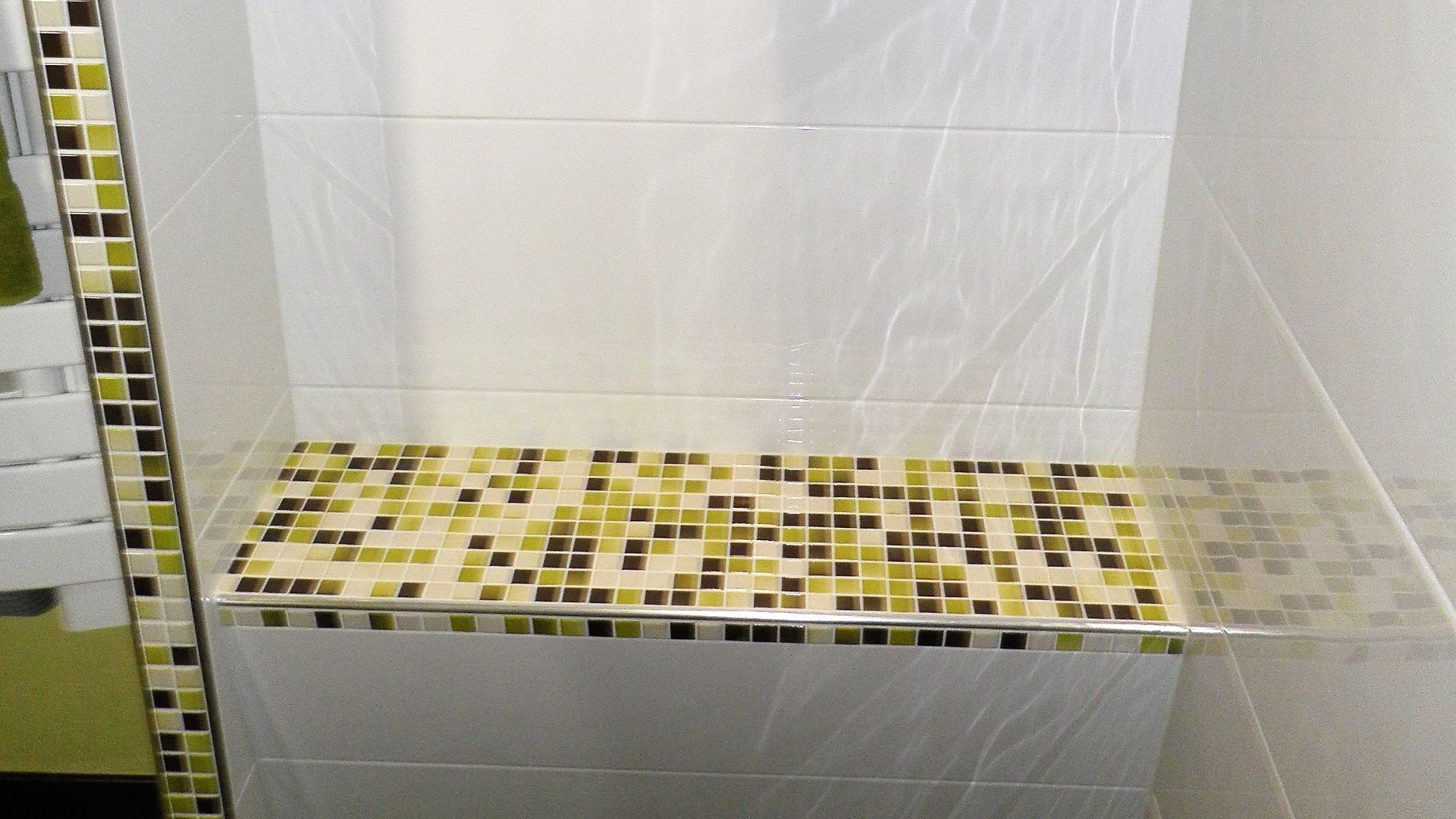 Alcôve de douche carrelée avec accents de mosaïque sur le banc et la frise verticale.