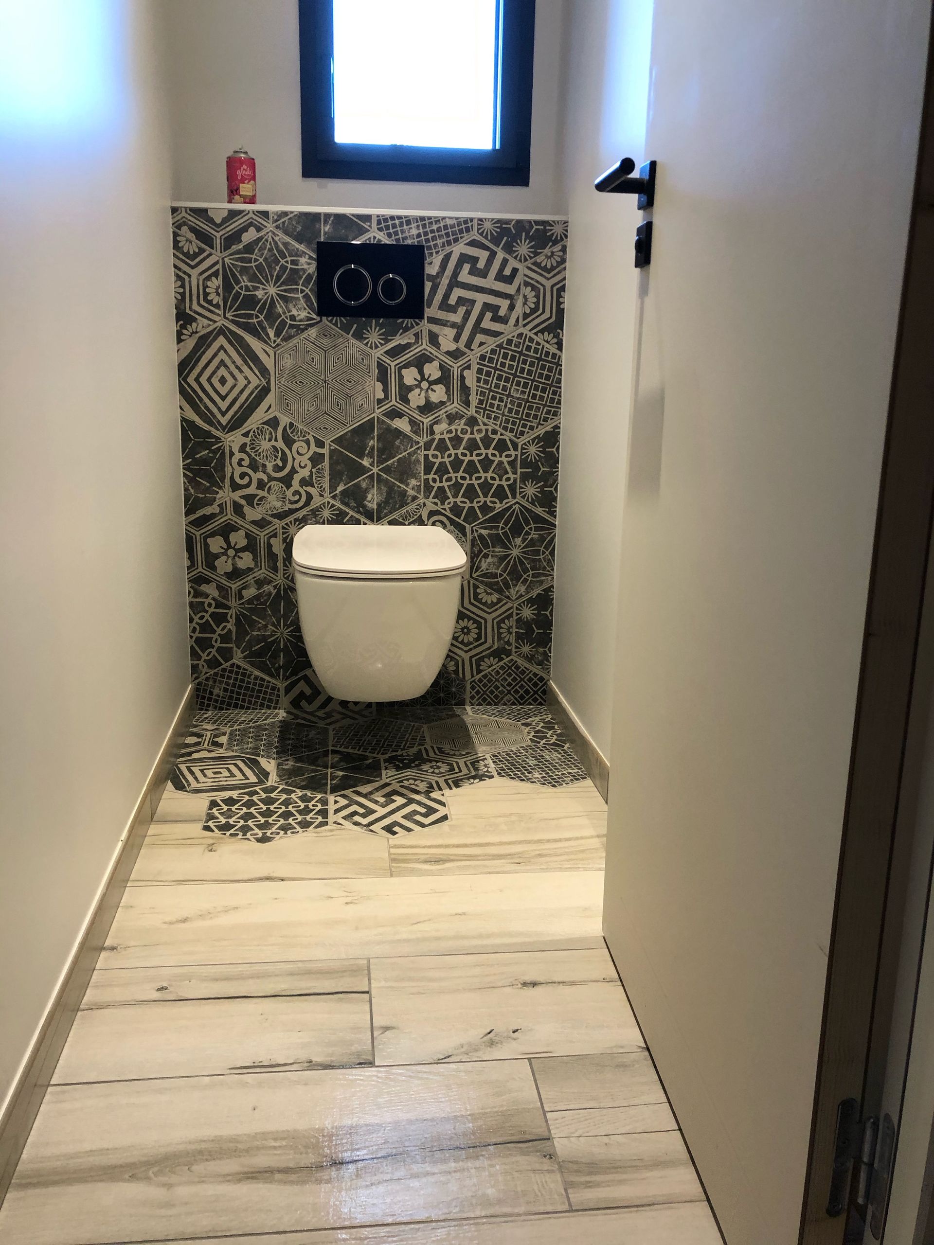 Toilettes modernes avec mur carrelé à motifs, toilettes suspendues et petite fenêtre au-dessus.